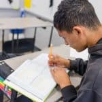 A young male student is writing in a notebook, immersed in his studies